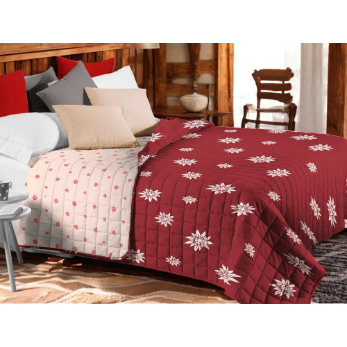 Colcha acolchada Edelweiss roja con flores blancas sobre cama rústica